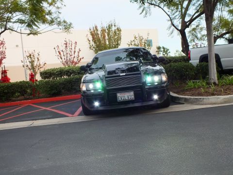 2003 Ford Crown Victoria - Lowered black sedan angled view, billet grille and halo projectors lit, custom front guard.