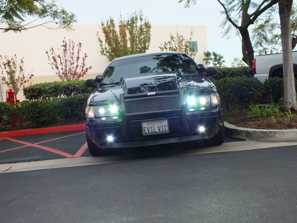 Black sedan with billet grille and push bar parked in lot, EVIL VIC California plate