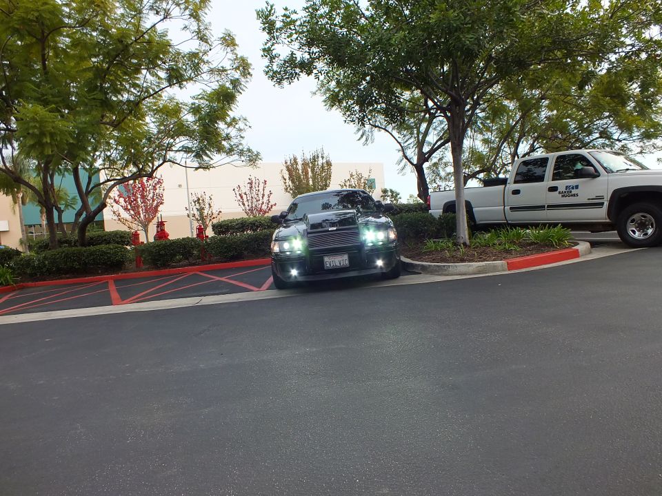 Distant black sedan with grille guard parked beside white pickup in parking lot
