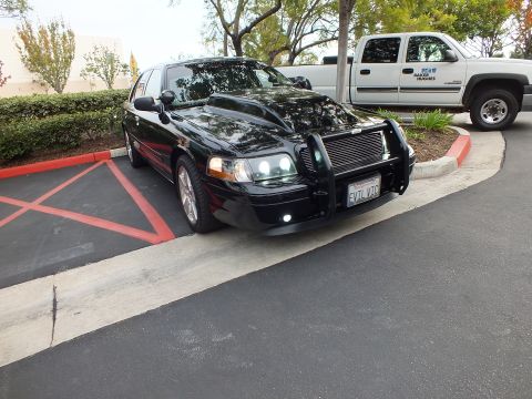 2003 Ford Crown Victoria - Lowered black sedan angled view showing push bar, side profile and chrome wheels near white truck.
