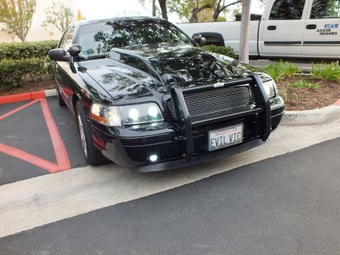2003 Ford Crown Victoria - Lowered black sedan angled view, custom front guard and billet grille, EVIL VIC plate, lot setting.