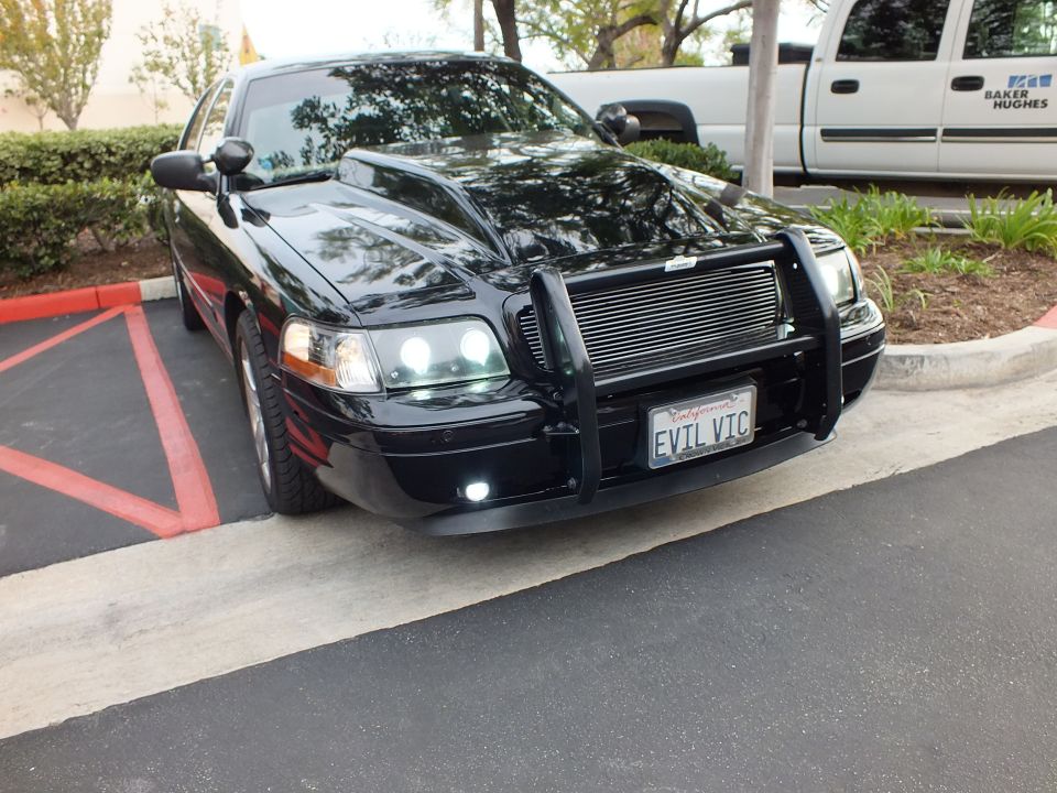 Black Crown Victoria side-front view with push bar and chrome wheels parked beside white van