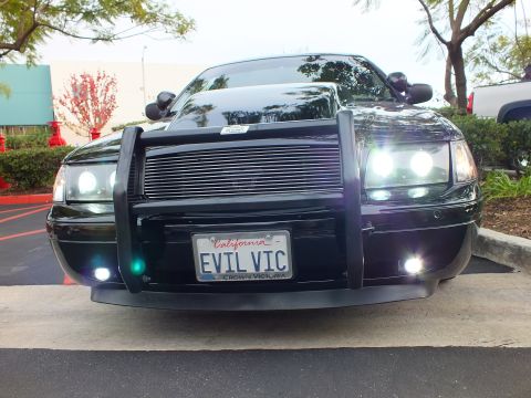 2003 Ford Crown Victoria - Front-on shot of lowered black sedan with custom guard; plate frame confirms Crown Victoria.