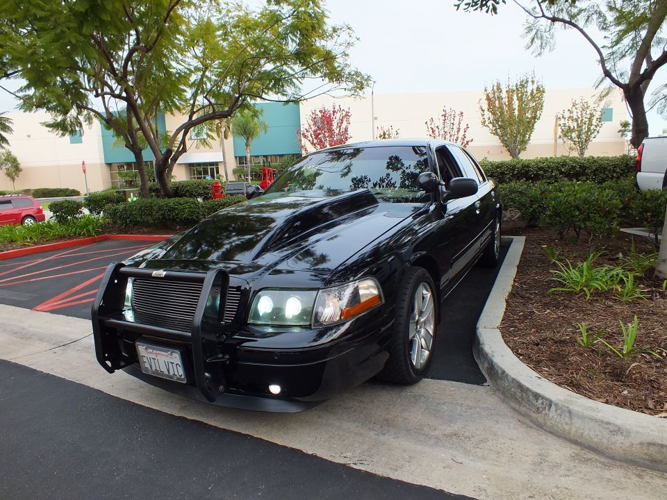 Black Crown Victoria sedan parked by landscaping with grille guard and aftermarket wheels