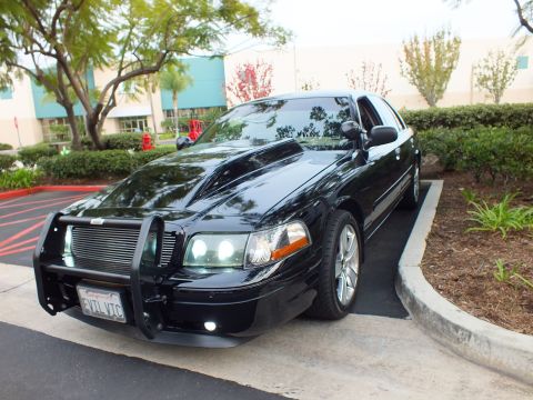 2003 Ford Crown Victoria - Front three-quarter view of a black Crown Victoria with billet grille, brush guard and projector headlights.