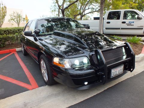 2003 Ford Crown Victoria - Black Ford Crown Victoria with grille guard parked beside a white Baker Hughes utility pickup.