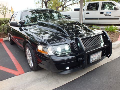 2003 Ford Crown Victoria - Black Crown Victoria front-quarter view with billet grille and EVL VIC plate, white pickup in background.