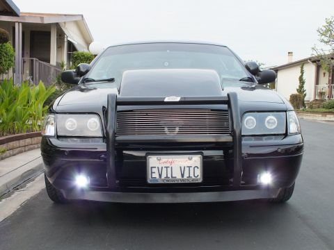 2003 Ford Crown Victoria - Black Crown Victoria photographed head-on with fog lights on, brush guard and EVIL VIC plate, in a neighborhood.