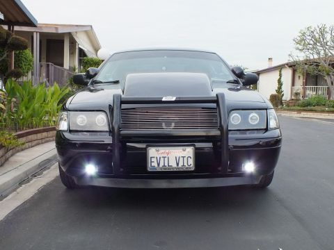 2003 Ford Crown Victoria - Head-on shot of a black Crown Victoria on a street, halo headlights and brush guard with EVIL VIC plate.