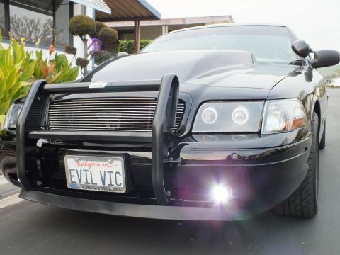 2003 Ford Crown Victoria - Front-quarter view of a black Crown Victoria with brush guard and a flaring fog light, EVIL VIC plate visible.