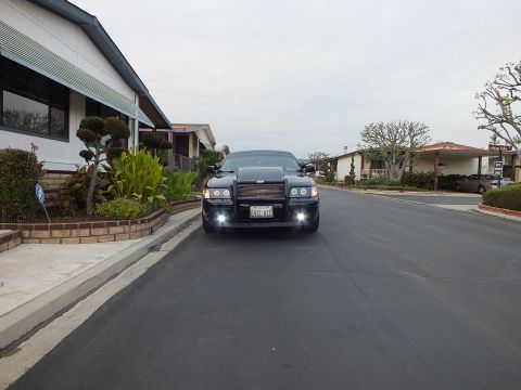2003 Ford Crown Victoria - Distant front view of a black Crown Victoria with fog lights lit, parked along a quiet residential street.