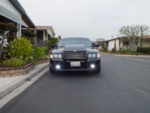 2003 Ford Crown Victoria - Black Crown Victoria viewed from the front on a street, brush guard and EVIL VIC plate, fog lights on.