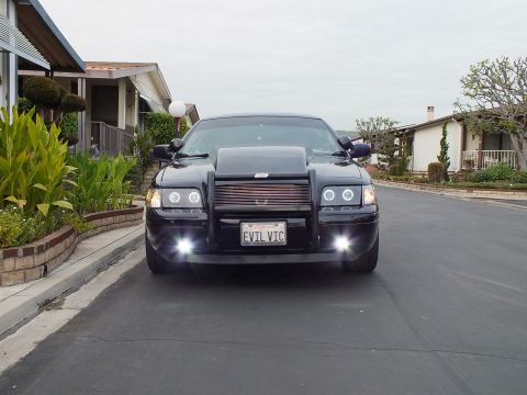 2003 Ford Crown Victoria - Front view of a black Crown Victoria with halo headlights and lit fog lamps on a residential street.