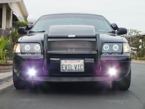 2003 Ford Crown Victoria - Tight head-on view of a black Crown Victoria, glowing halo headlights and flaring fog lamps, EVIL VIC plate.