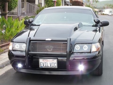 2003 Ford Crown Victoria - Front-quarter view of a black Crown Victoria with halo headlights and fog lamps, hills in the background.