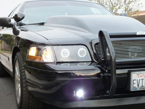 2003 Ford Crown Victoria - Detail of a black Crown Victoria left front: halo projector headlight, amber signal, brush guard and fog lamp.