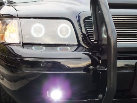 2003 Ford Crown Victoria - Detail of dual halo rings and a glowing LED fog light on a black Ford sedan with chrome billet grille.