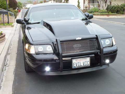 2003 Ford Crown Victoria - Head-on shot of a black Crown Victoria on a residential street, push bar guard and halo headlights lit.