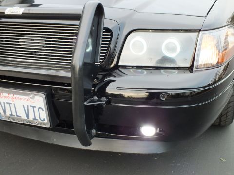 2003 Ford Crown Victoria - Detail of the chrome billet grille and black push bar beside a lit halo headlight on a Crown Victoria.