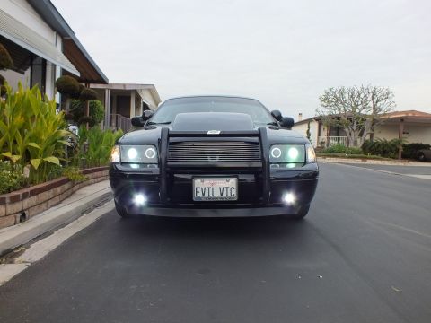 2003 Ford Crown Victoria - Low front view of a black Crown Victoria on pavement, push bar and halo headlights lit at dusk.
