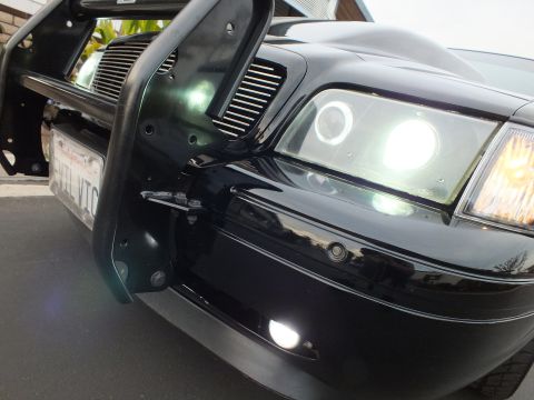 2003 Ford Crown Victoria - Low-angle detail of a Crown Victoria's lit halo headlight, black push bar and chrome billet grille.