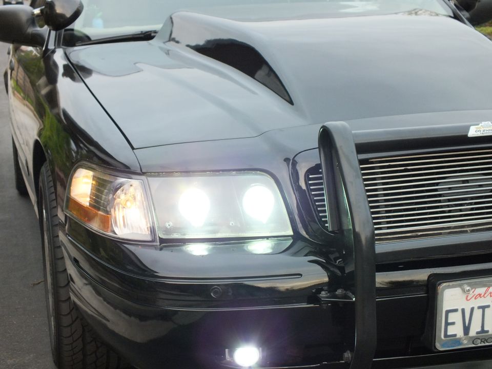 Black Crown Victoria front quarter with hood scoop and lit headlights