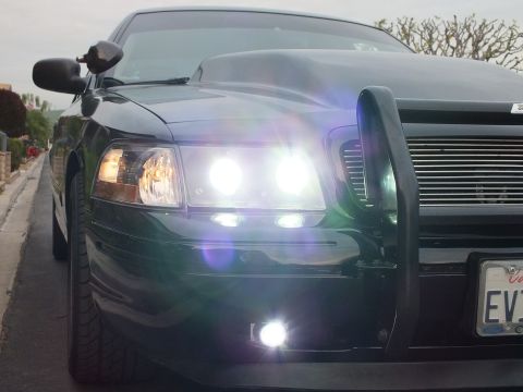 2003 Ford Crown Victoria - Headlights and fog lamps illuminated on a black Crown Victoria with a black grille guard at dusk.