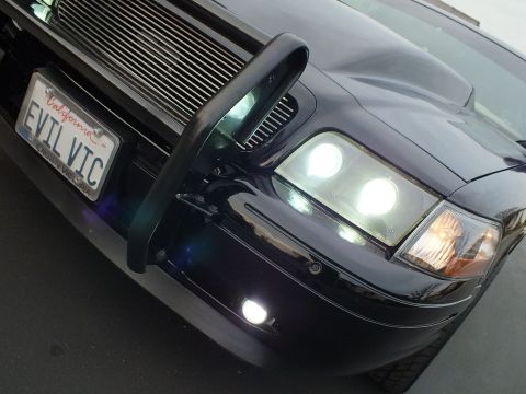 2003 Ford Crown Victoria - Close view of glowing halo headlights and a chrome billet grille behind a black push bar.