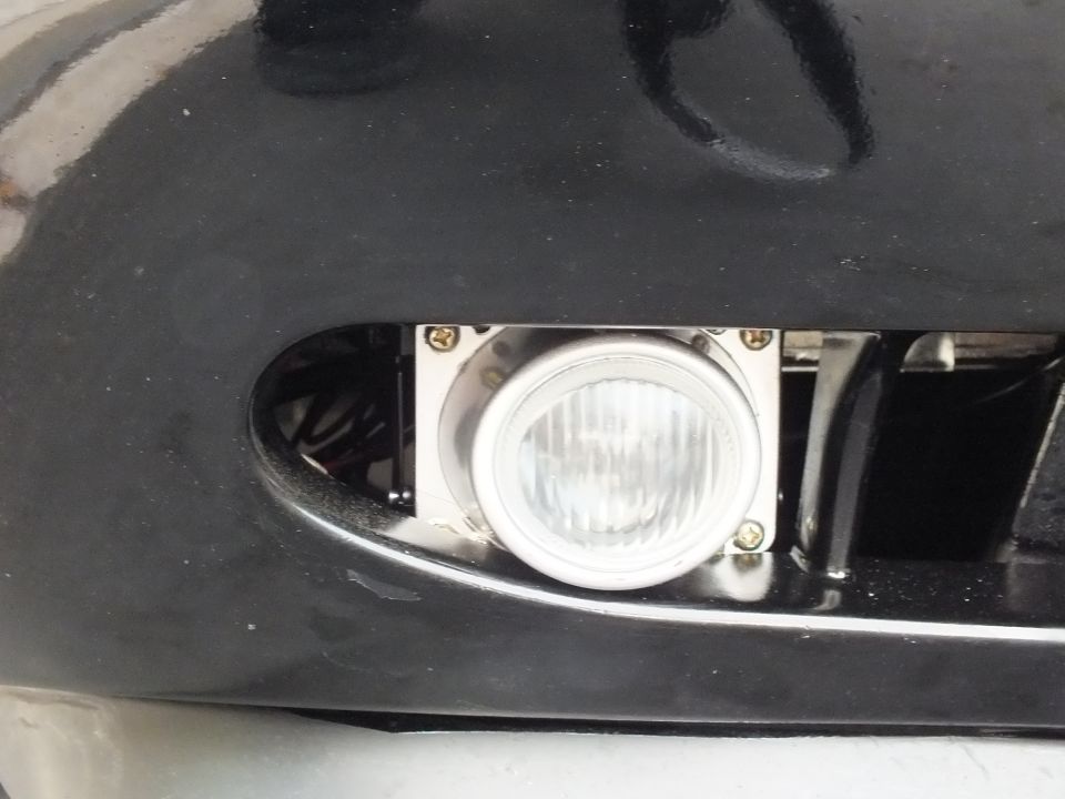 Round chrome-bezel fog lamp set into black bumper beside billet grille
