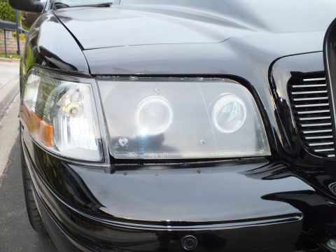 2003 Ford Crown Victoria - Low-angle view of the headlight halos and chrome grille on a black Crown Victoria.