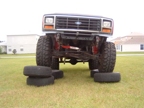 1983 Ford Bronco - A lifted Ford Bronco sits on stacked tires, its front end and suspension modifications.