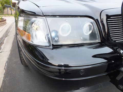 2003 Ford Crown Victoria - Side-on view of the headlight halos and chrome grille on a glossy black sedan.