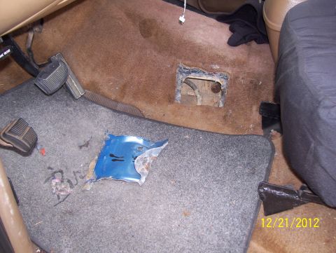 1990 Ford Bronco - The interior floor of a vehicle shows damage and wear, with exposed metal and torn carpeting.