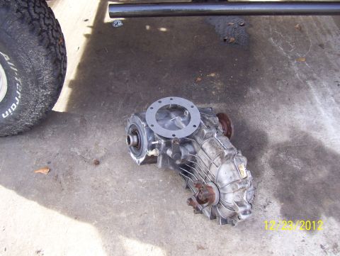 1990 Ford Bronco - A transfer case sits on a concrete surface next to a tire and part of a vehicle frame.