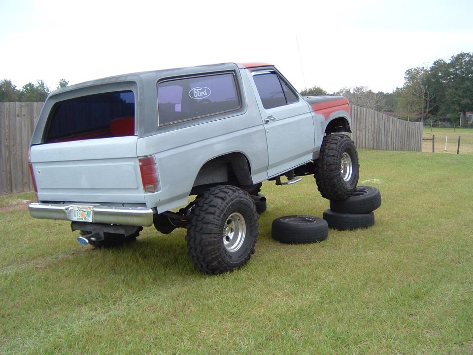 Primer-gray lifted Ford Bronco flexing suspension over stacked tires on mud-terrain tires