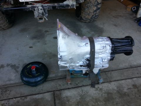 1978 Ford Bronco - A transmission and torque converter are displayed on a stand, with the rear of a vehicle in the background.