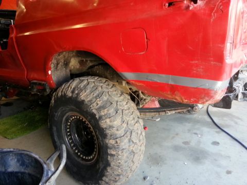 1978 Ford Bronco - Rear view of a red pickup truck with a large off-road tire, showing the quarter panel and suspension.