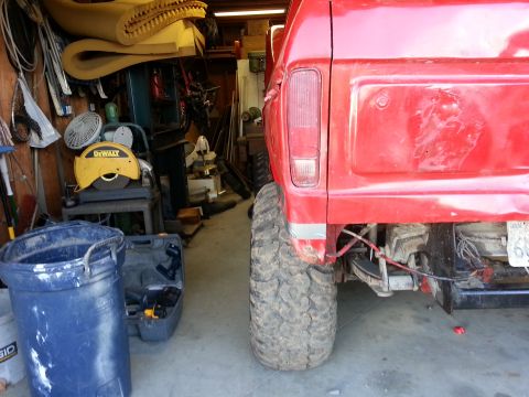 1978 Ford Bronco - The rear of a red pickup truck is shown in a cluttered garage setting, with large off-road tires visible.