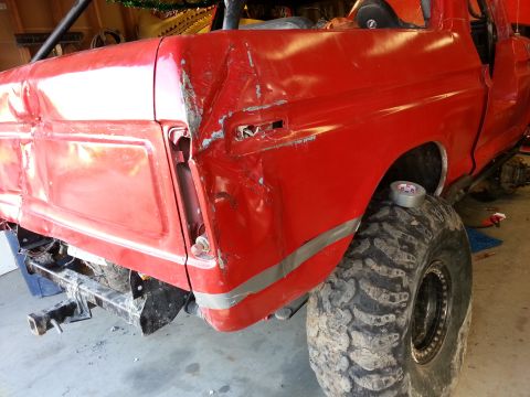 1978 Ford Bronco - The rear of a red pickup truck shows extensive damage, with a large off-road tire and a roll bar visible.