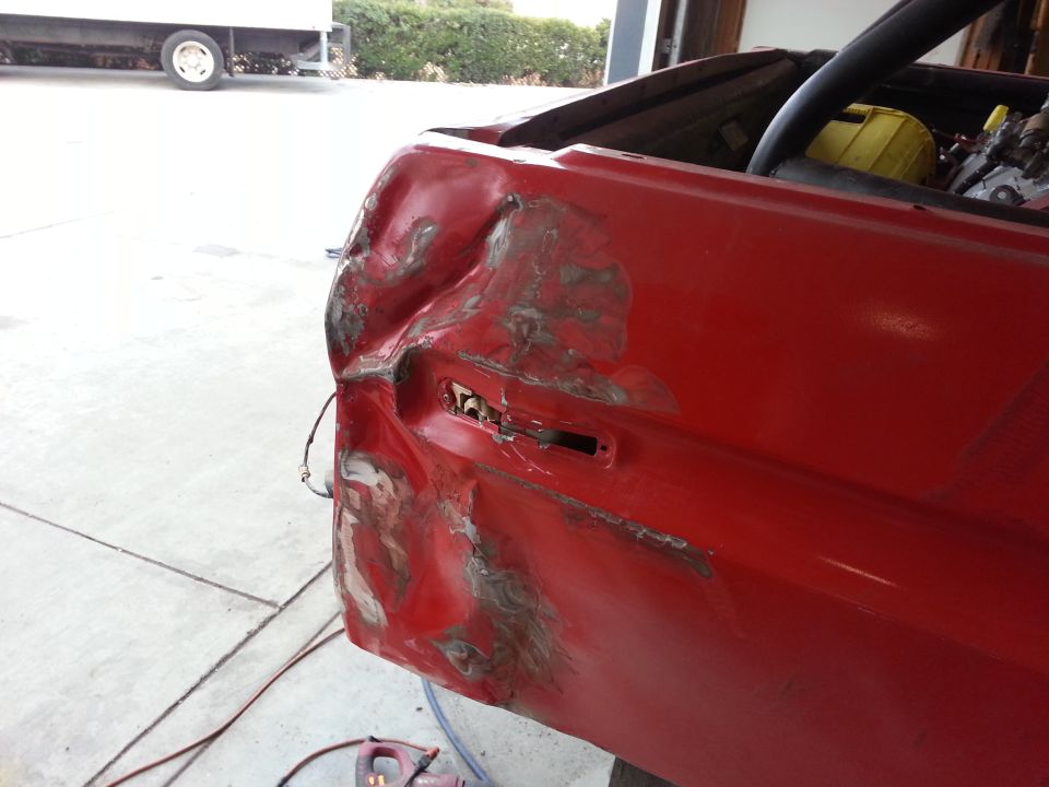 Heavily dented red rear quarter panel of a vehicle, showing rust and primer