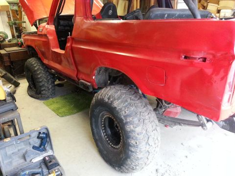 1978 Ford Bronco - A red 1978 Ford Bronco is shown in a garage with its hood up and large off-road tires.