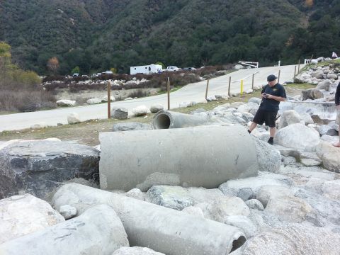 1978 Ford Bronco - Concrete pipes and rocks are scattered around a road in a hilly, natural landscape.