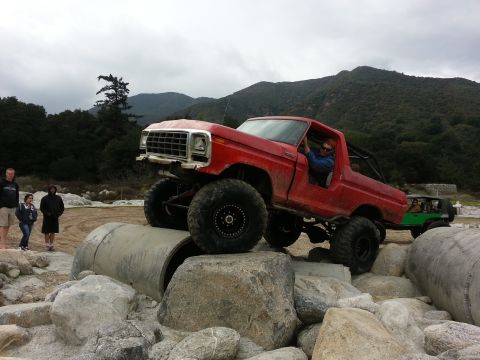 1978 Ford Bronco - A red off-road truck navigates a rocky obstacle course with another vehicle following behind.