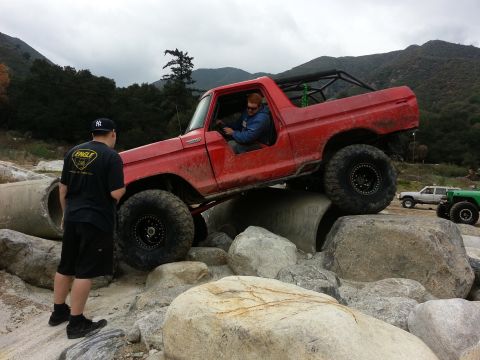 1978 Ford Bronco - A red 1978 Ford Bronco navigates a challenging off-road course with large rocks and concrete obstacles.