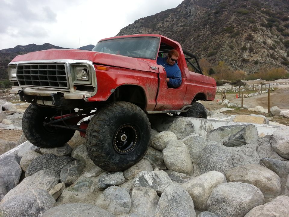 red pickup truck with big tires going over rocks, driver in blue jacket