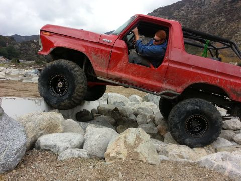 1978 Ford Bronco - A red 1978 Ford Bronco is shown off-roading over large rocks with a driver inside.
