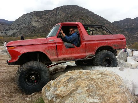 1978 Ford Bronco - Driver maneuvers a red 1978 Ford Bronco over large rocks during an off-road excursion.