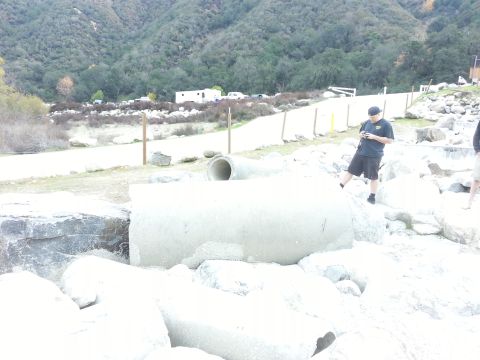 1978 Ford Bronco - A man stands on rocks near a large concrete pipe in a natural setting with parked vehicles visible in the distance.
