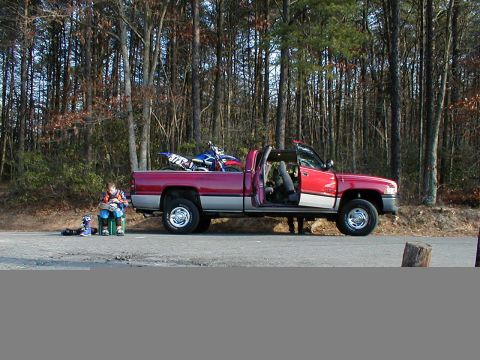 1995 Ford Bronco - A red and grey pickup truck is parked on the side of a road with a dirt bike loaded in the bed.