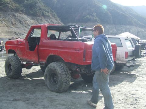 1978 Ford Bronco - A red 1978 Ford Bronco, heavily modified for off-road use with oversized tires, is parked outdoors next to other vehicles.
